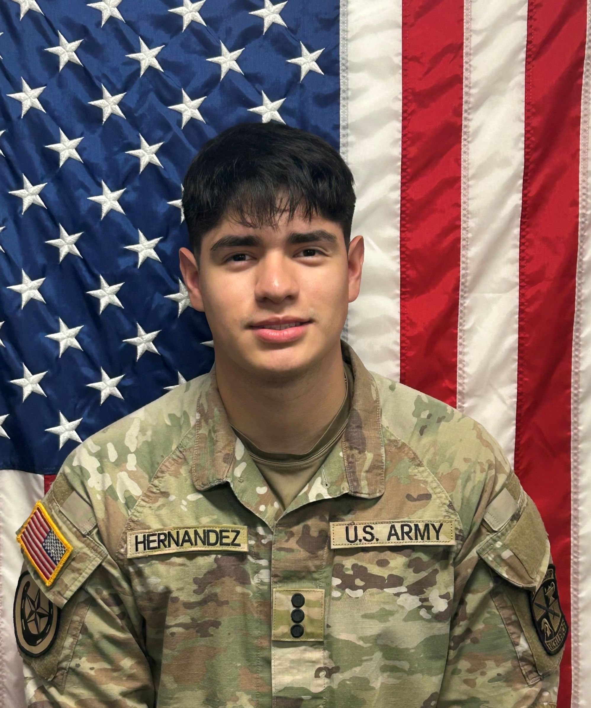 Cadet Hernandez standing in front of a U S A flag in uniform.