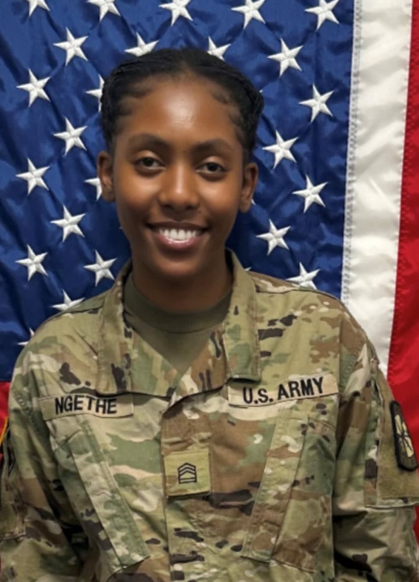 Cadet Ngethe standing in front of a U S A flag in uniform.