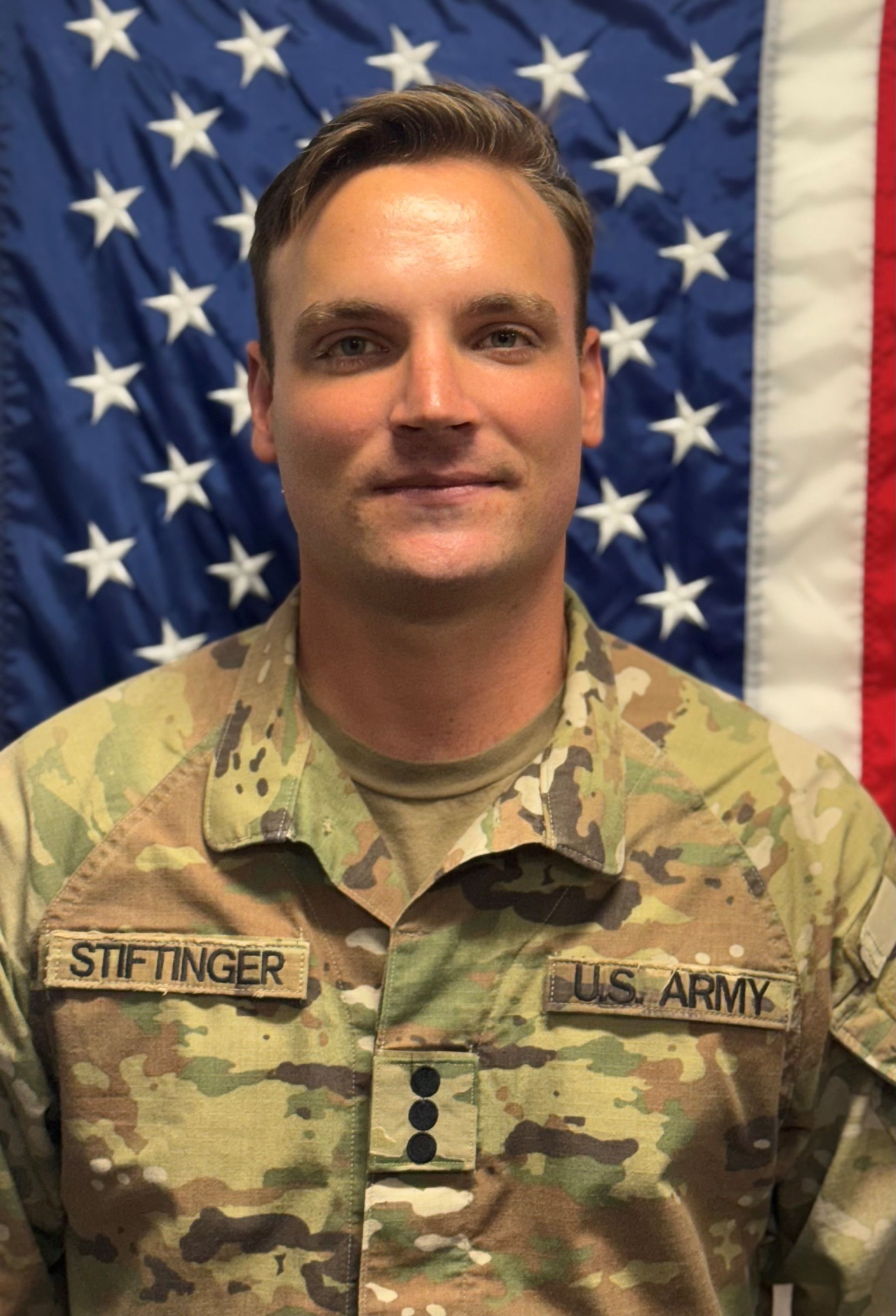 Cadet Stiftinger standing in front of a U S A flag in uniform.
