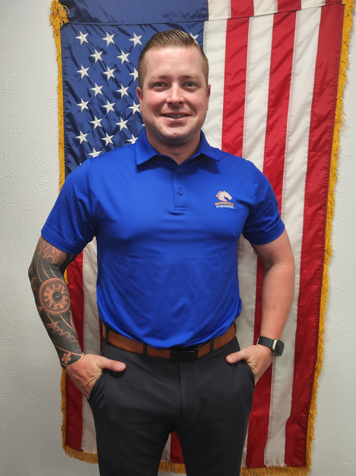 SFC Kyle Kuchelmeister standing in front of the U S flag, wearing a U T A shirt.