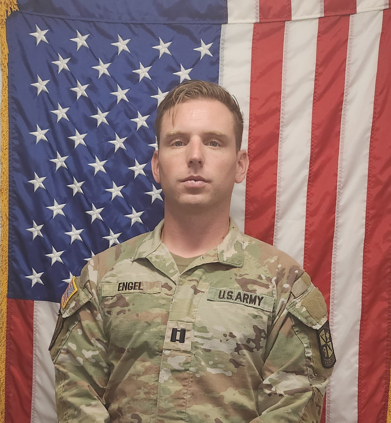 CPT Benjamin Engel standing in front of the American flag.