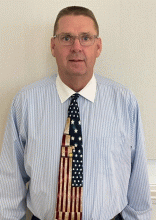 Matthew Giddings wearing a button down, a tie that resembles the U S flag, and glasses.