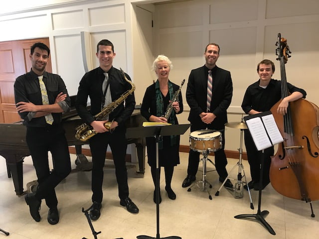 Five people standing with instruments, smiling at the camera.