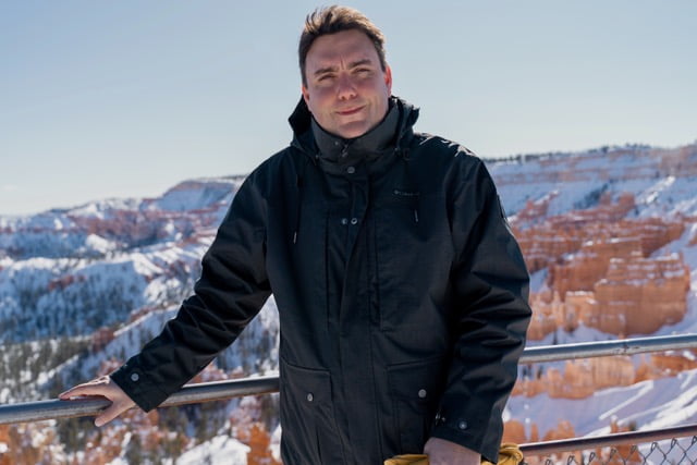 Jeremy Byrd wearing a heavy jacket with snowy mountains behind him