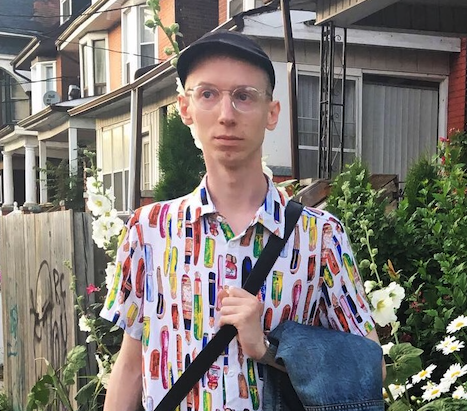 Luke Roelofs  wearing a beret, glasses, colorful shirt, and a cross-body bag.