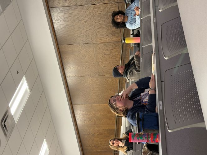 A group of students sitting in a classroom facing forward and listening to the speaker.