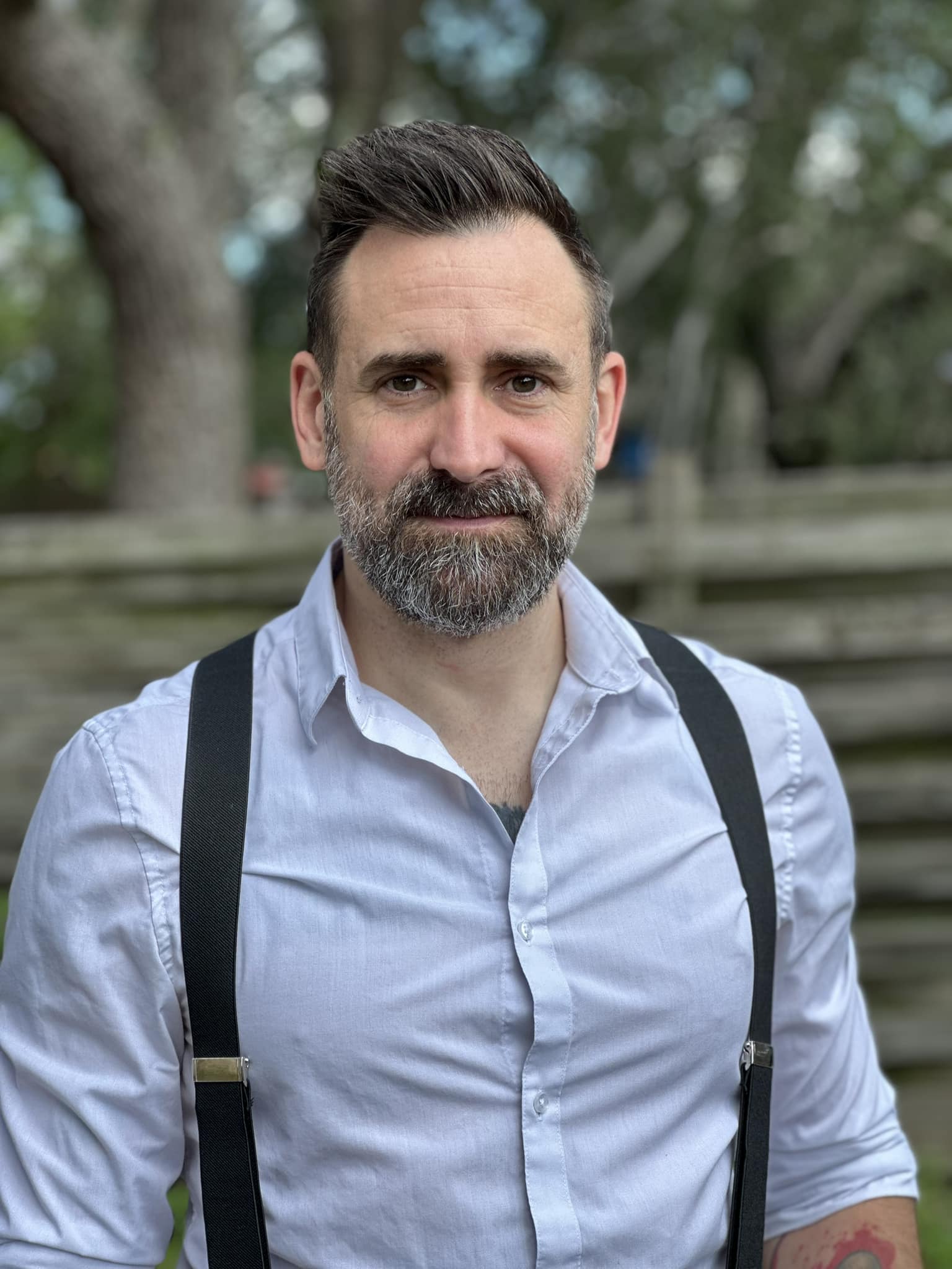 Adam Johnson headshot. He has short hair and a beard, wearing a button up and suspenders.