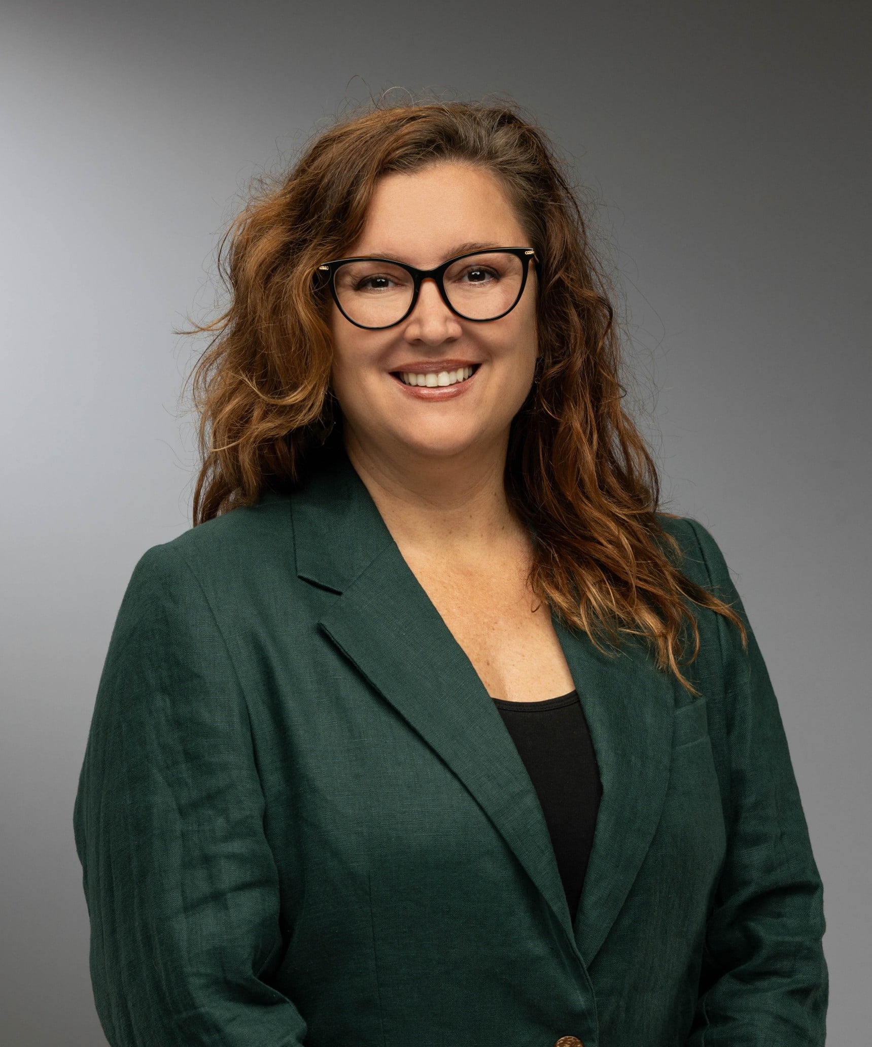 Andrea Kay's smiling wearing glasses, a plain shirt, and a blazer.