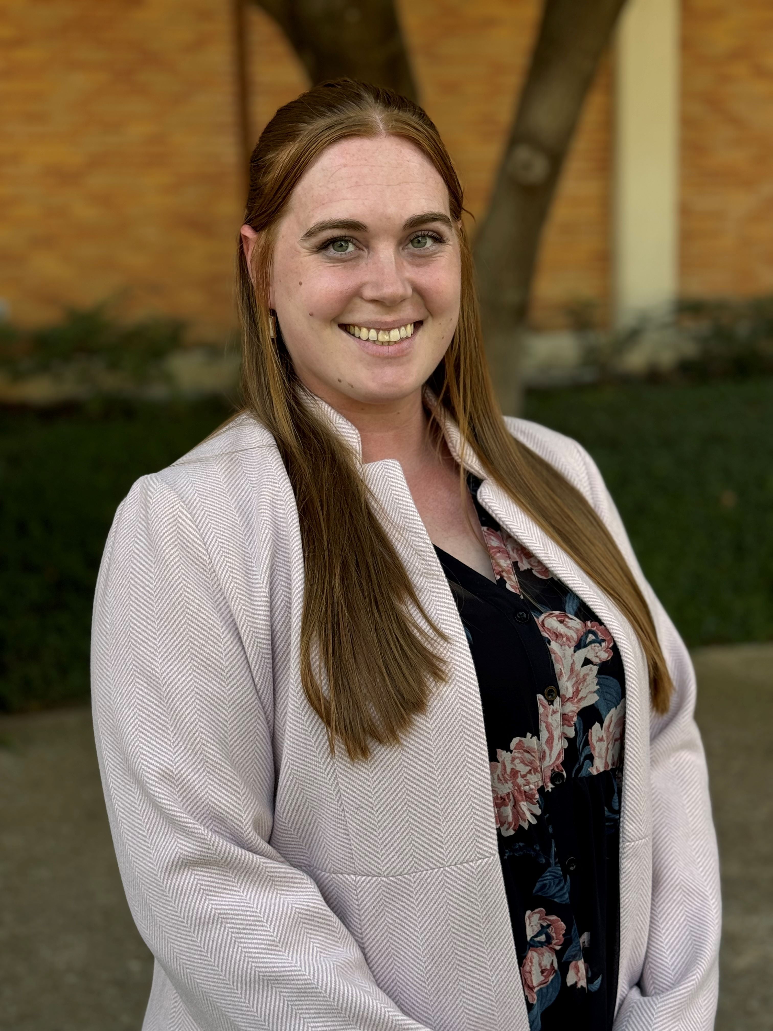 Julianna Adams smiling with long hair, a jacket, and patterned blouse.
