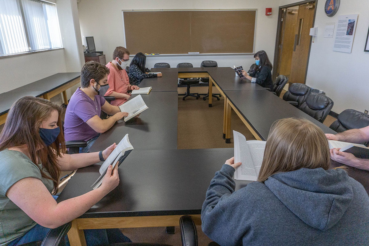 A set of people reading book in a meeting room with masks on." _languageinserted="true