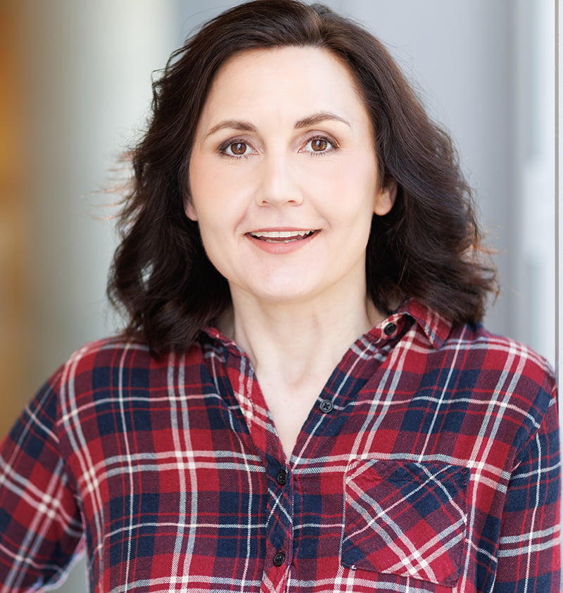 Alice Nelson headshot with shoulder length dark brown hair and red and blue plaid shirt.