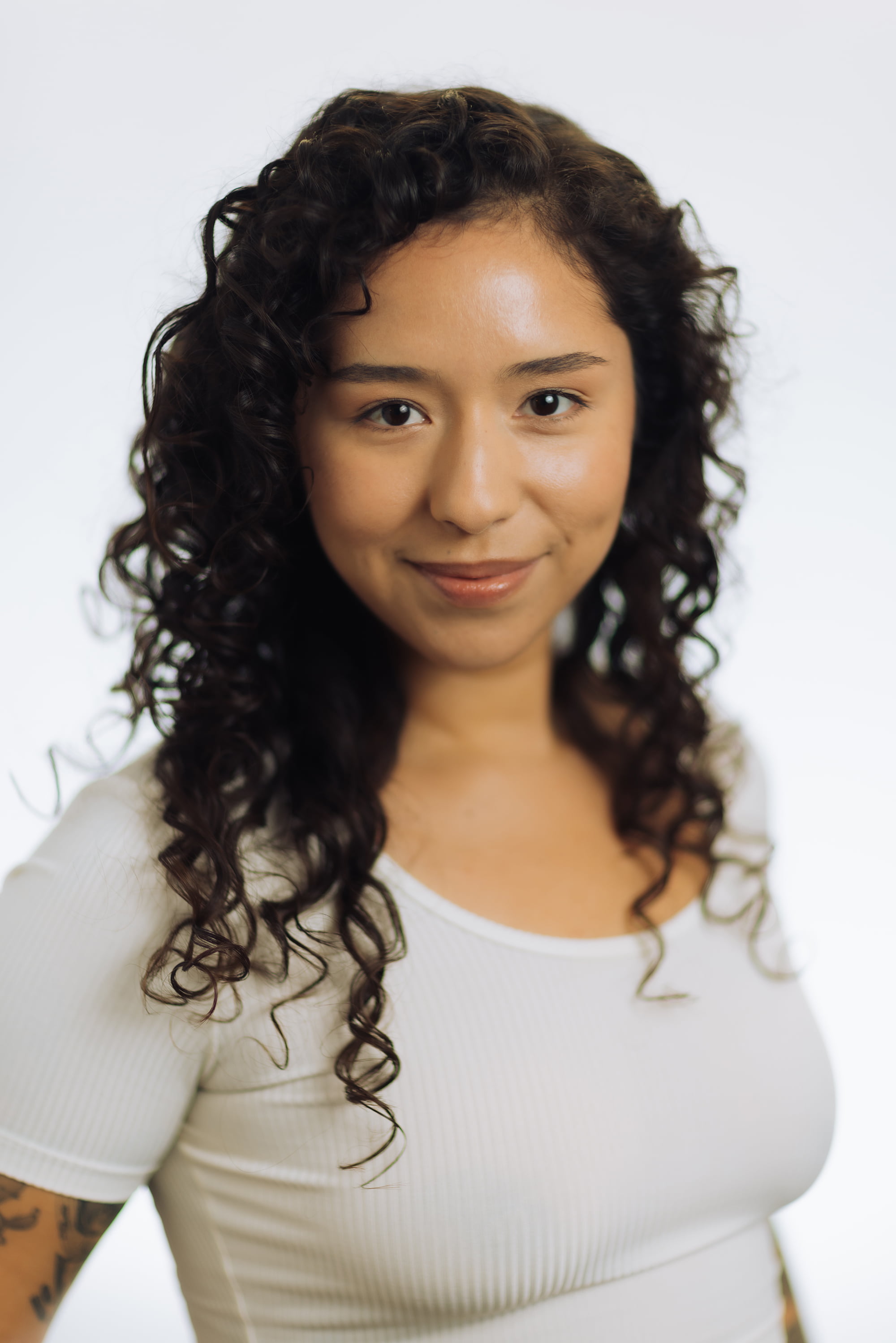 Woman in white shirt and dark, long curly hair smiling at camera.