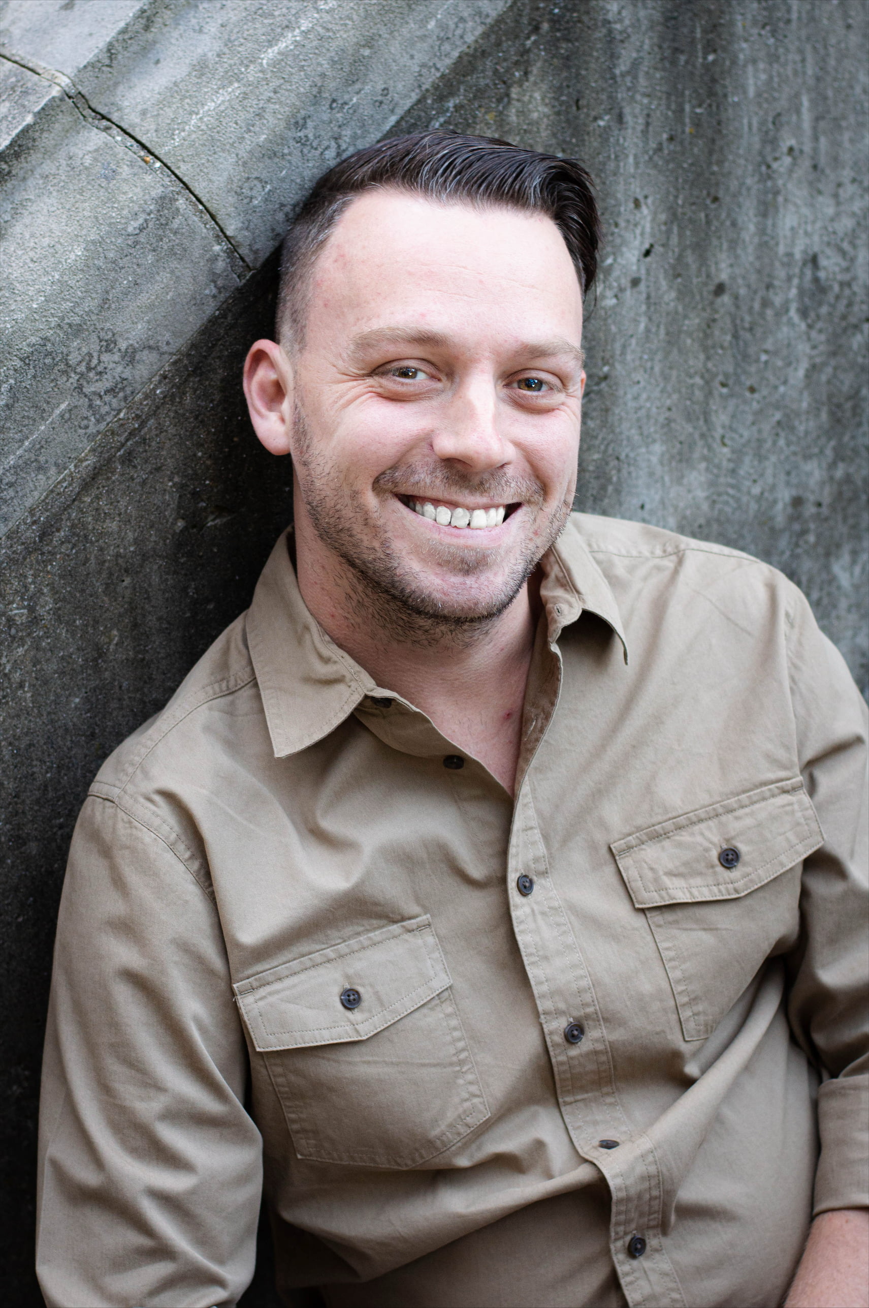 Man in tan shirt with short hair smiling at camera