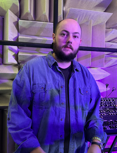 Man in blue shirt with sound equipment behind him