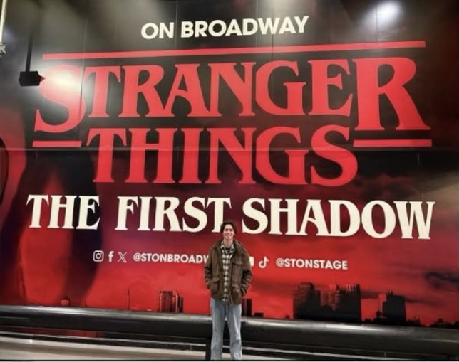 Ben standing in front of a giant sign for Stranger Things: The First Shadow on Broadway.