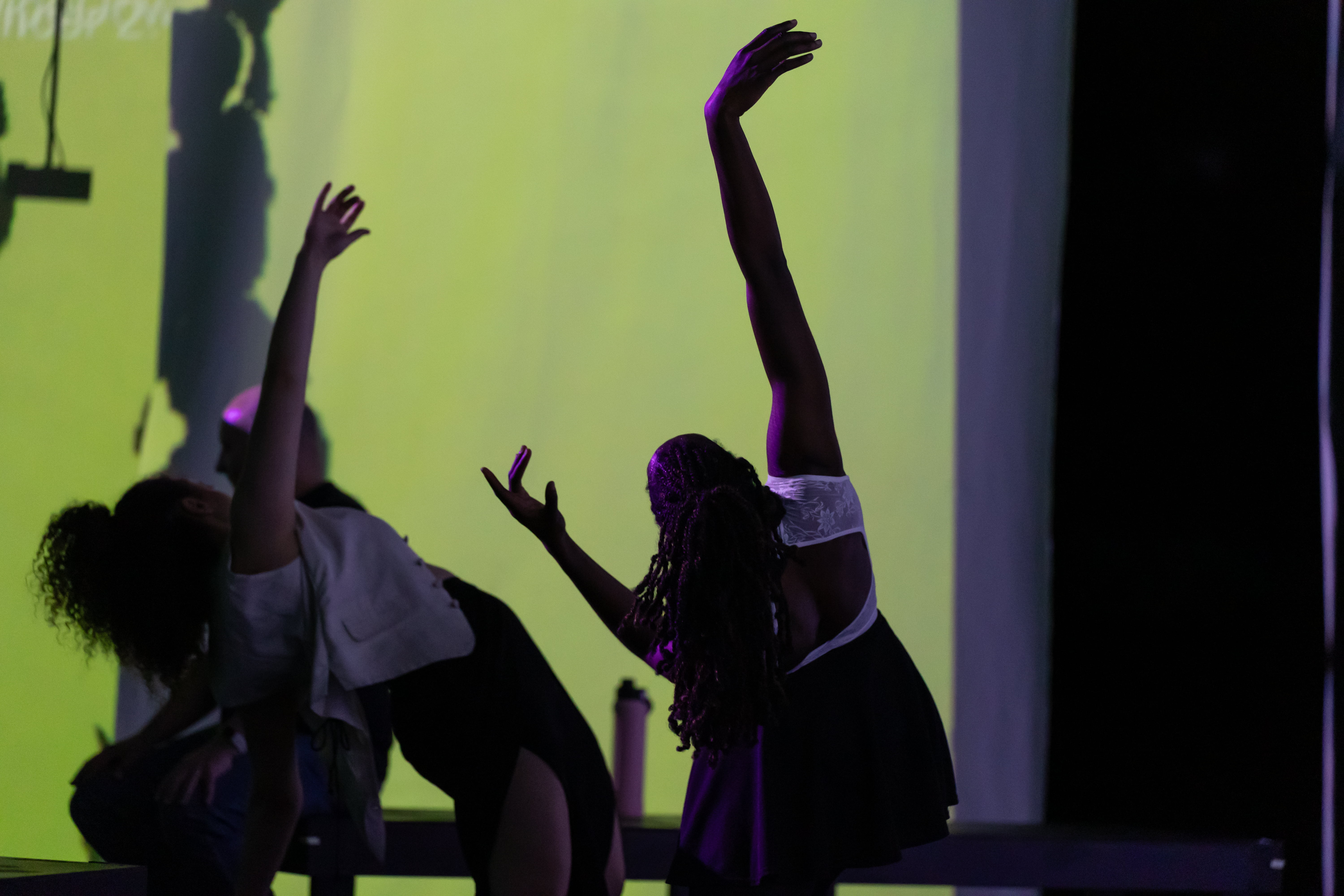 dancers leaning back with arms up in front of green light