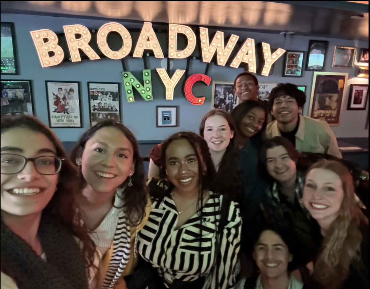 a group of excited students under a lighted sign that reads Broadway NYC