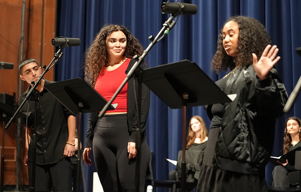Three actors at microphones in front of stage curtain