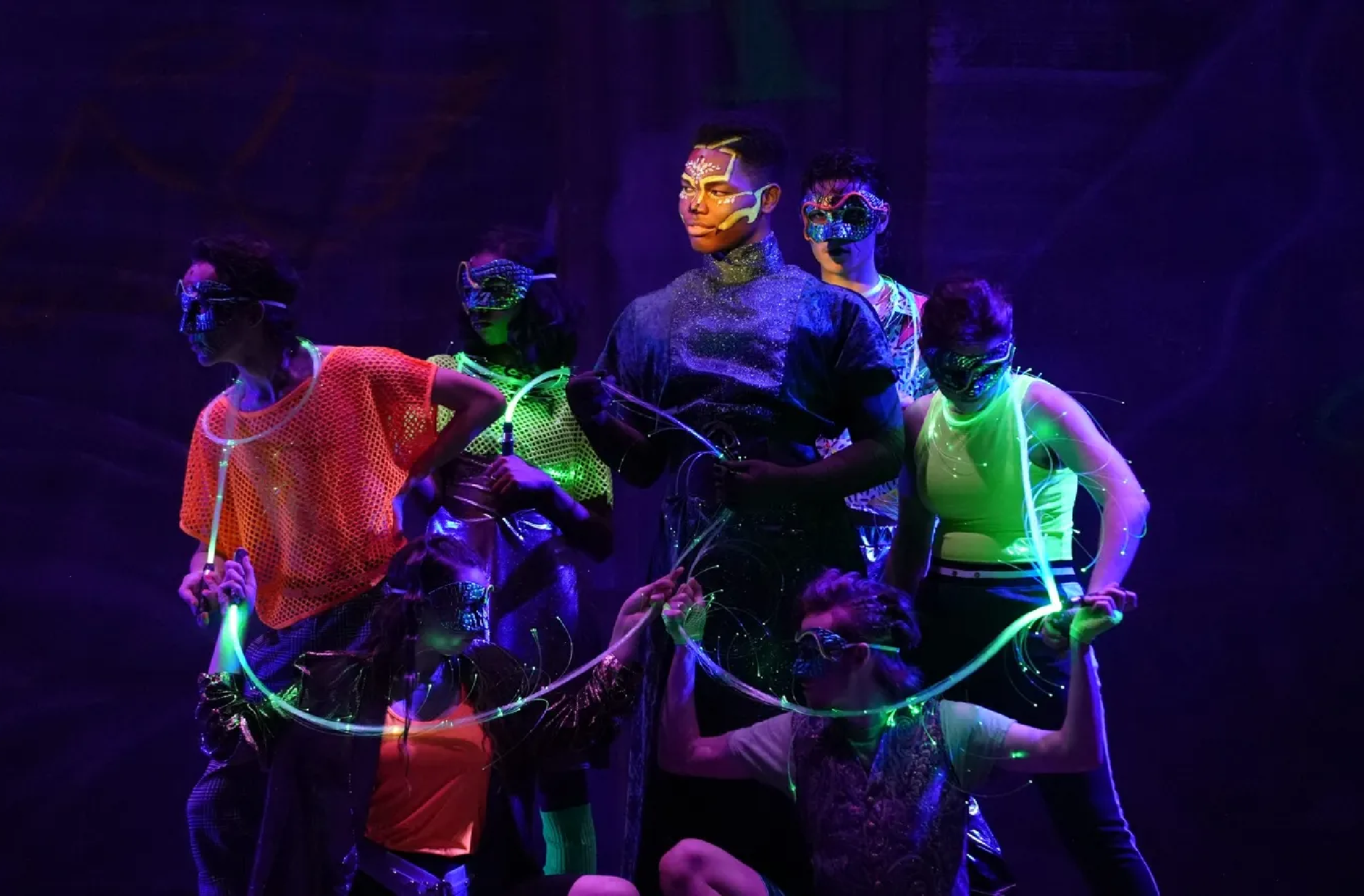 Seven performers in neon glow in the dark costumes and makeup.
