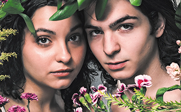 Two young people's faces peering out from flowers and leaves.