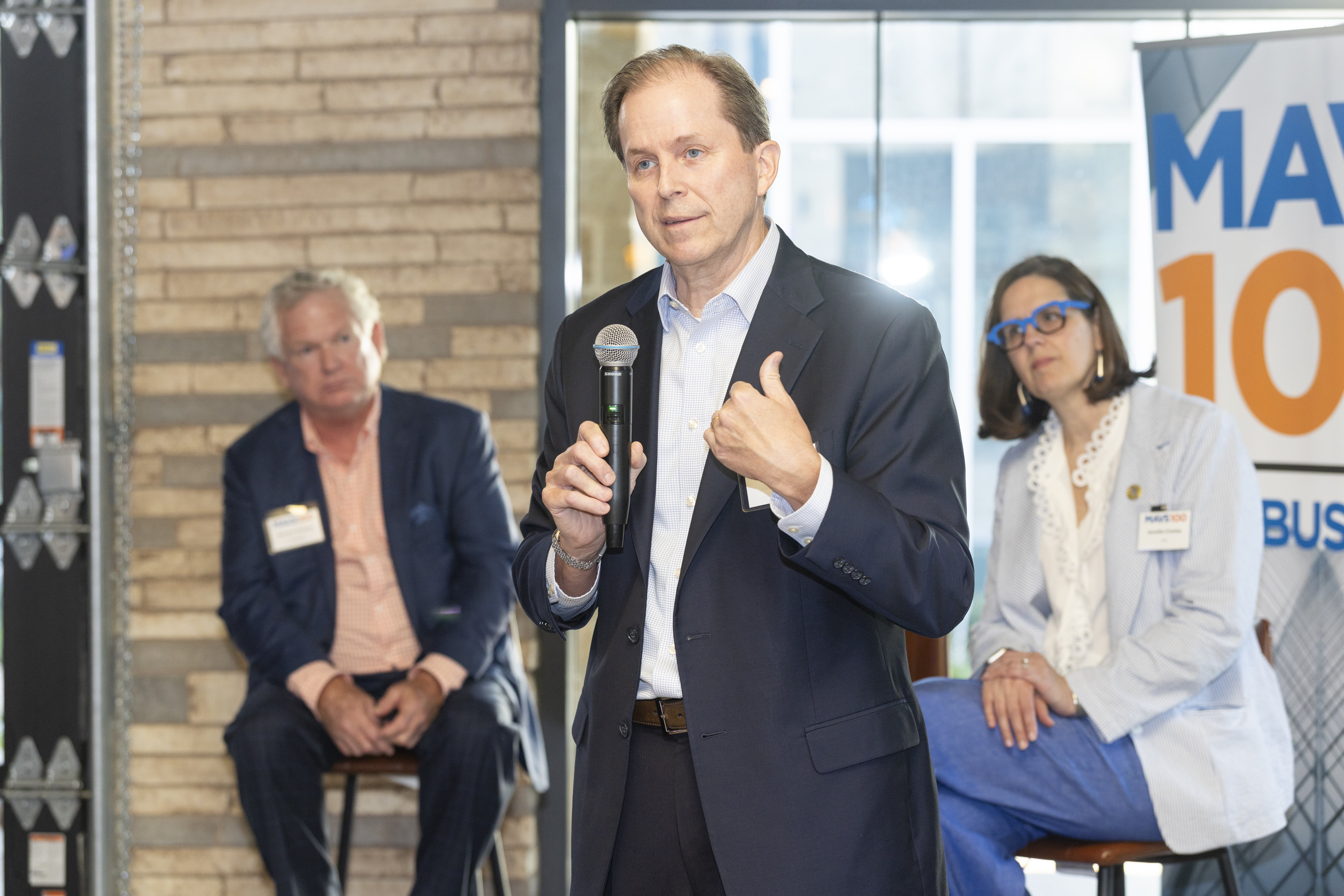 Amegy Bank Texas President and UTA alumnus Laif Afseth speaks into a microphone during a panel. Behind him, UTA President Jennifer Cowley and Amegy Bank Fort Worth President Brandon Bledsoe look on.