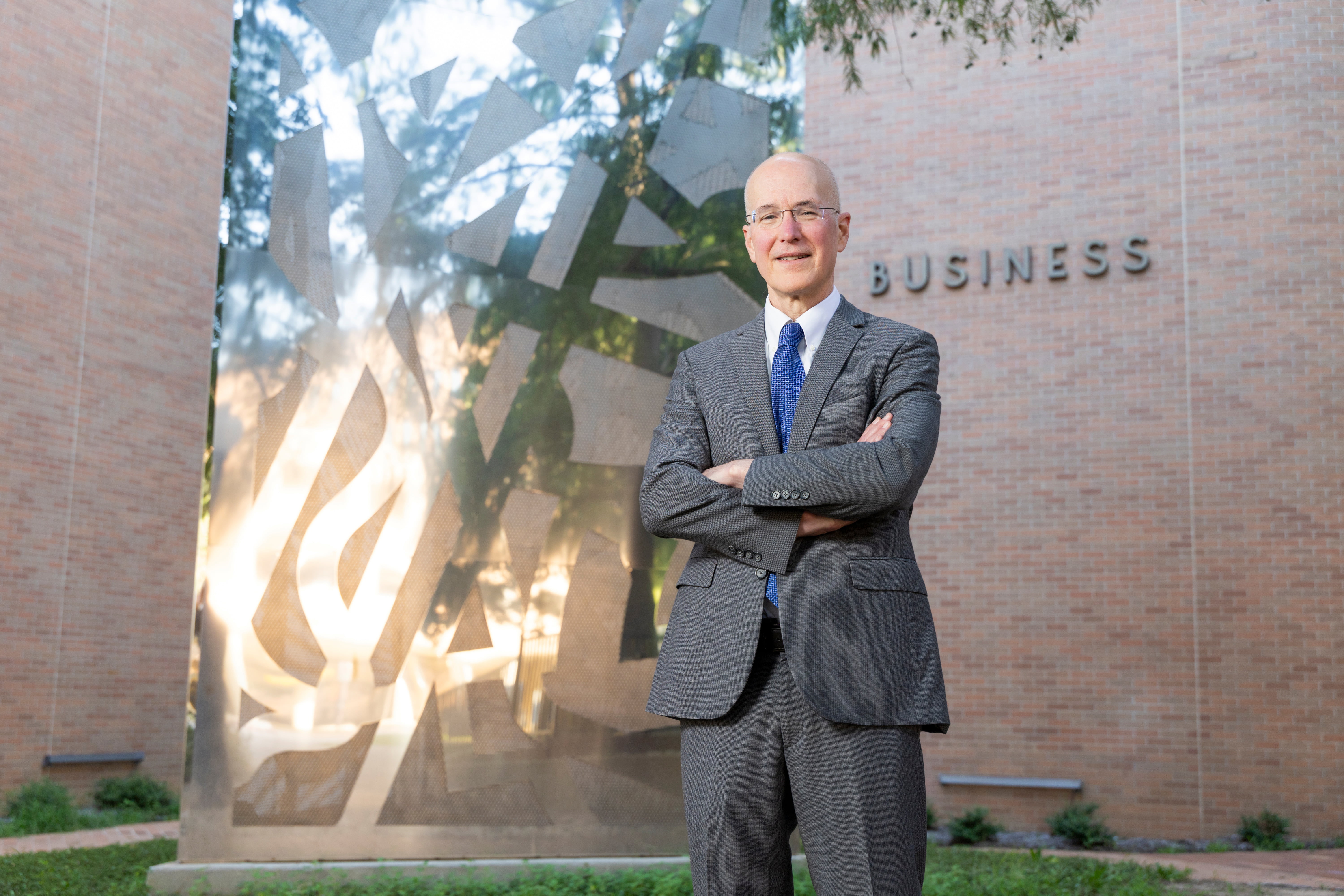 Dean Brian Klaas smiles with his arm crossed in front of the UTA College of Business building. 