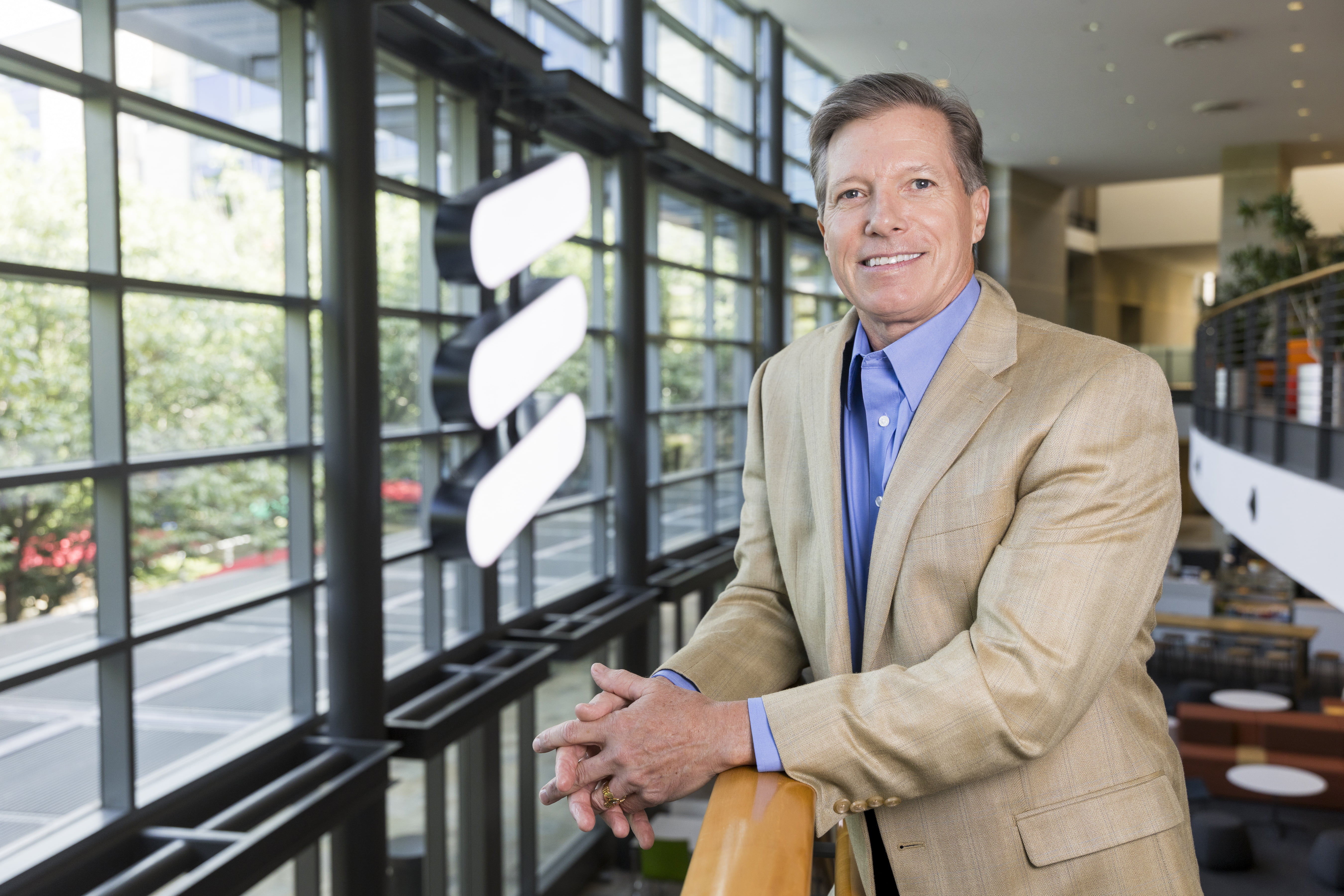 Brian White poses for a headshot. He is leaning against a rail, with the Ericsson logo illuminated behind him. Photo by Sharon Ellman. 