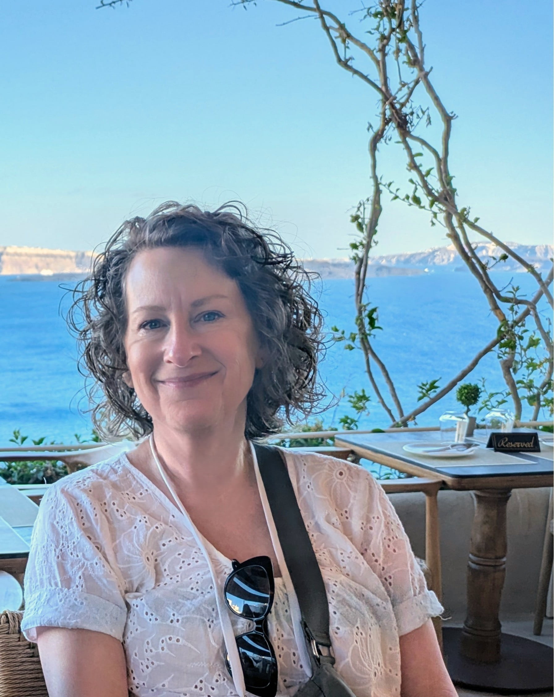 Catherine Hinton poses for a picture at a restaurant with the ocean view behind her in Santorini, Greece.