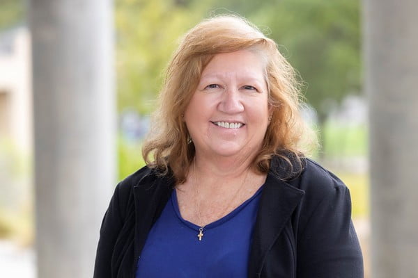 Denise Wylie poses for a headshot outside in front of trees. 