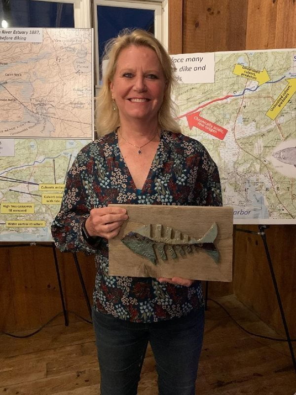 Jackie Fouse poses with a conservation award. The award features a mosaic blue and grey image of a fish on a rectangular wooden block.
