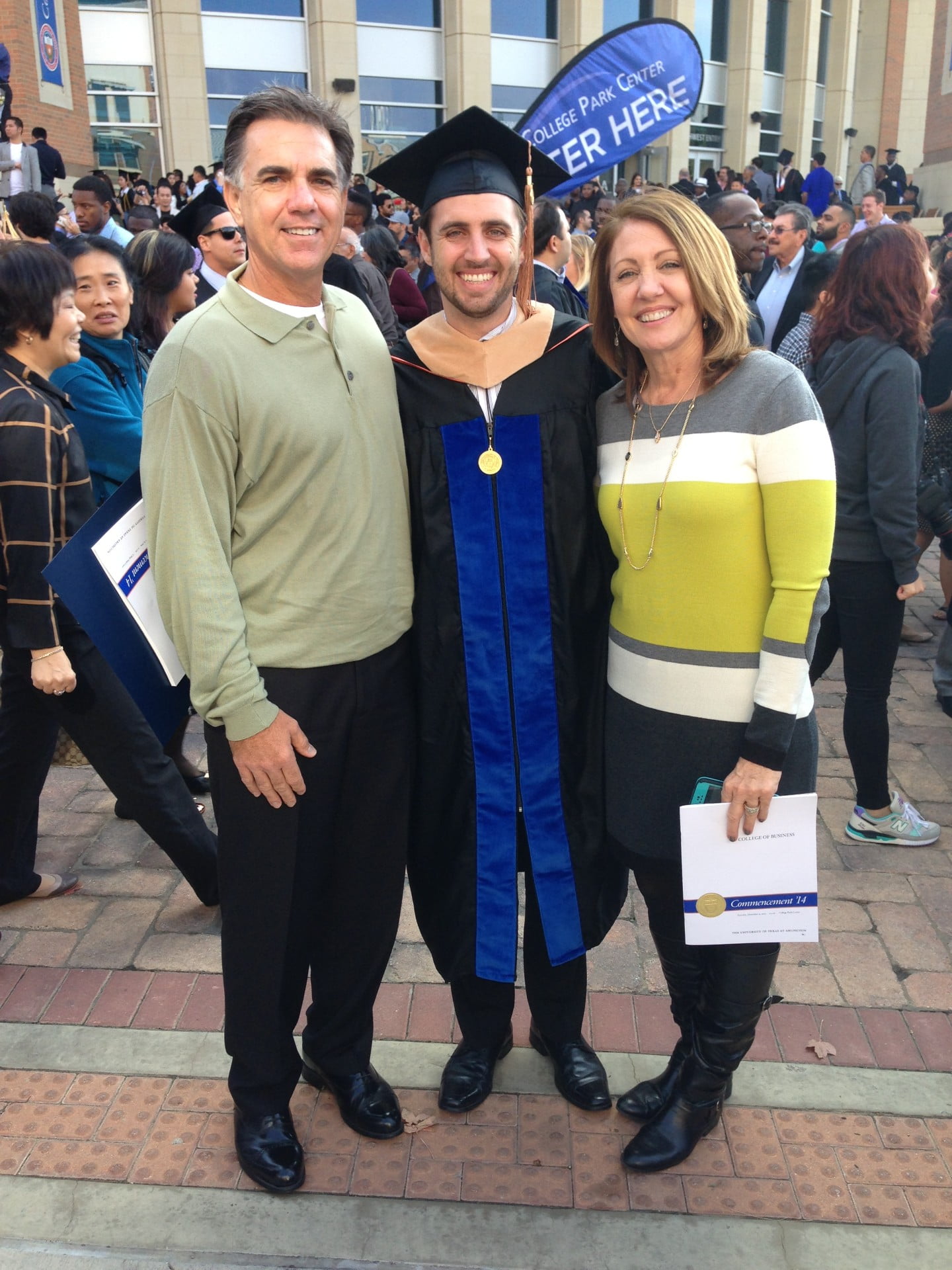 Jake Bailey poses with his parents. Jake is dressed in UTA MBA graduation apparel, with his parents on either side. 