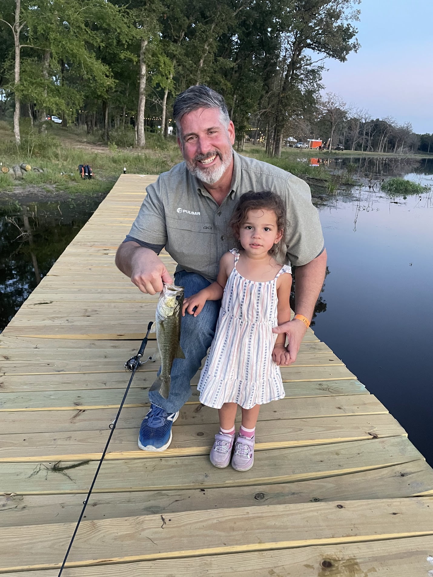 James Sellers smiles in a photo with his daughter. In it, they are on a dock on the lake, with James holding up a fish.