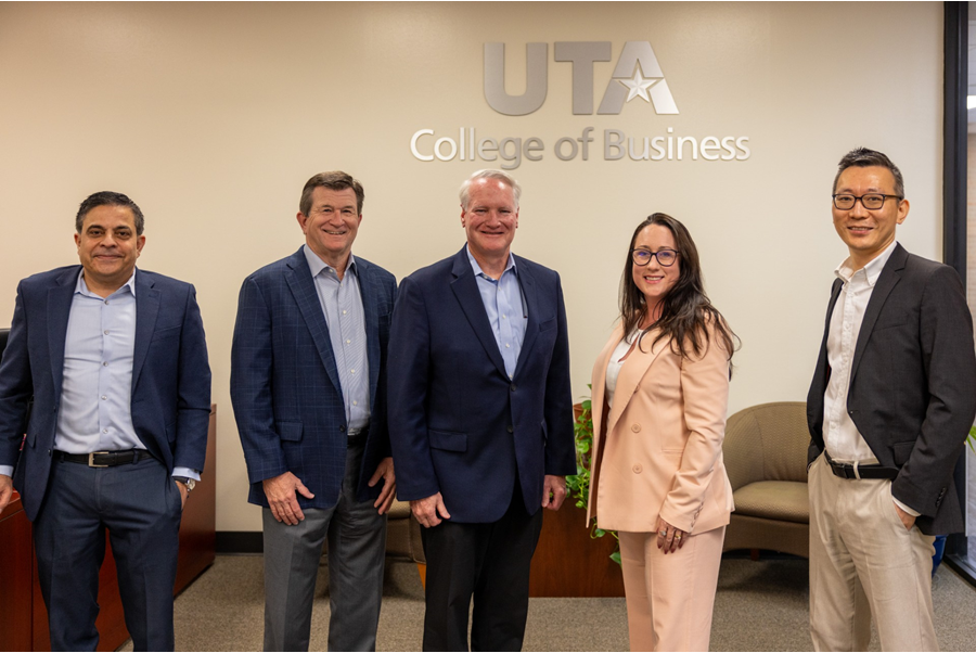 From left to right: Dr. Sanjiv Sabherwal, Dean Harry Dombroski, Rick Jenkins, Lacy Samples and Dr. Ten Wang. The group poses together for a photo, with the UTA College of Business logo on the wall behind them.