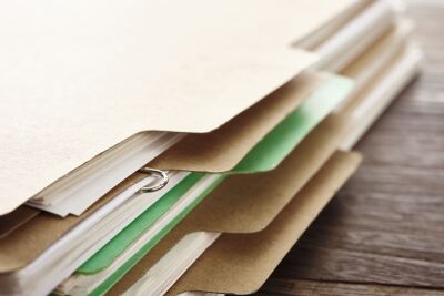 Stack of brown folders with visible pages and green inserts, resting on a wooden surface.