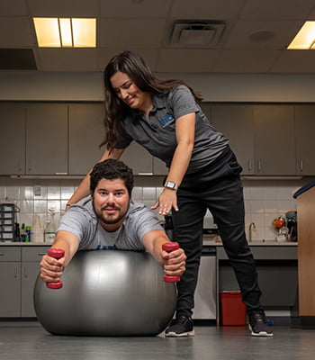female athletic training student assisting student balancing on medicine ball