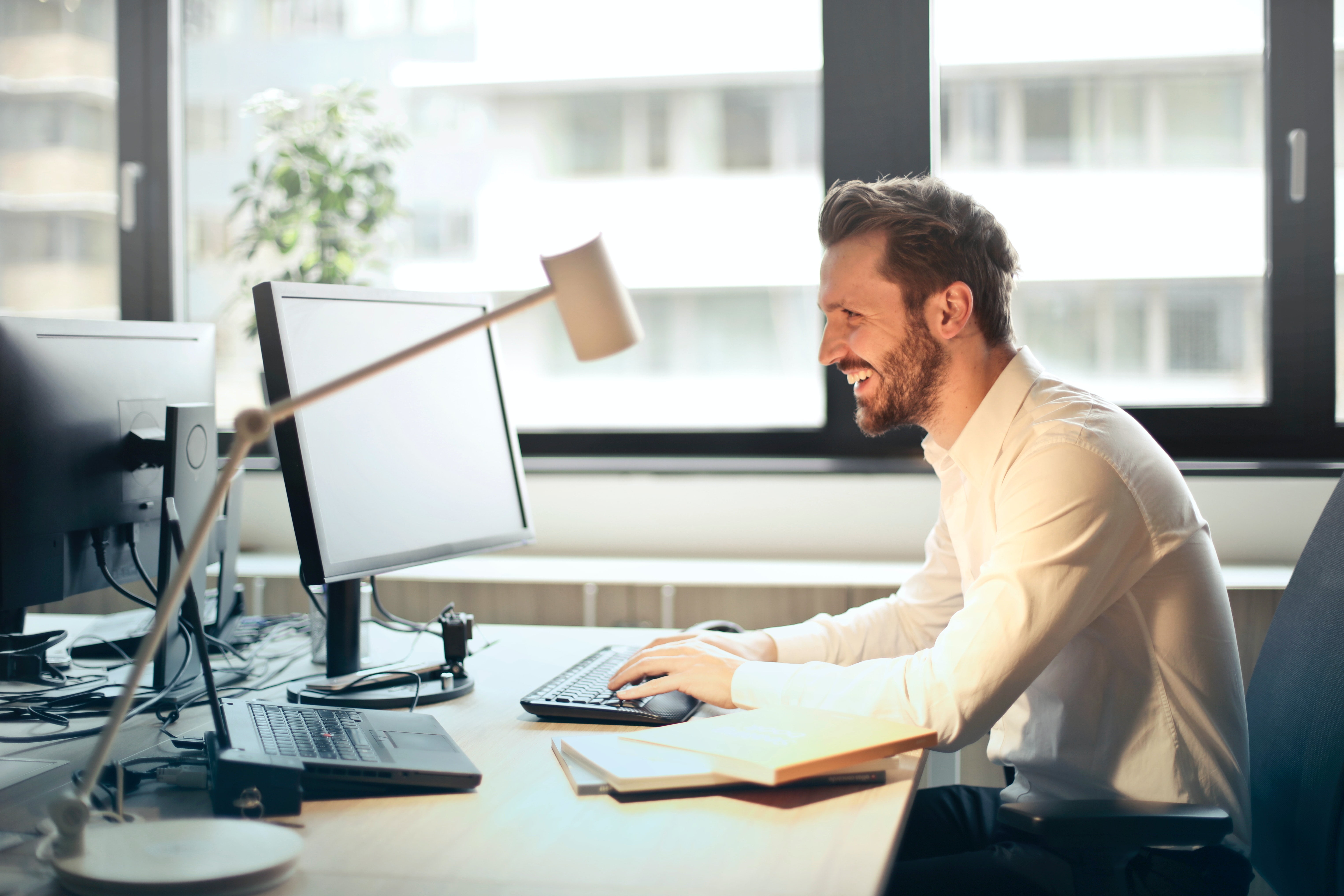 A person smiles while working on a laptop at his desk. 
