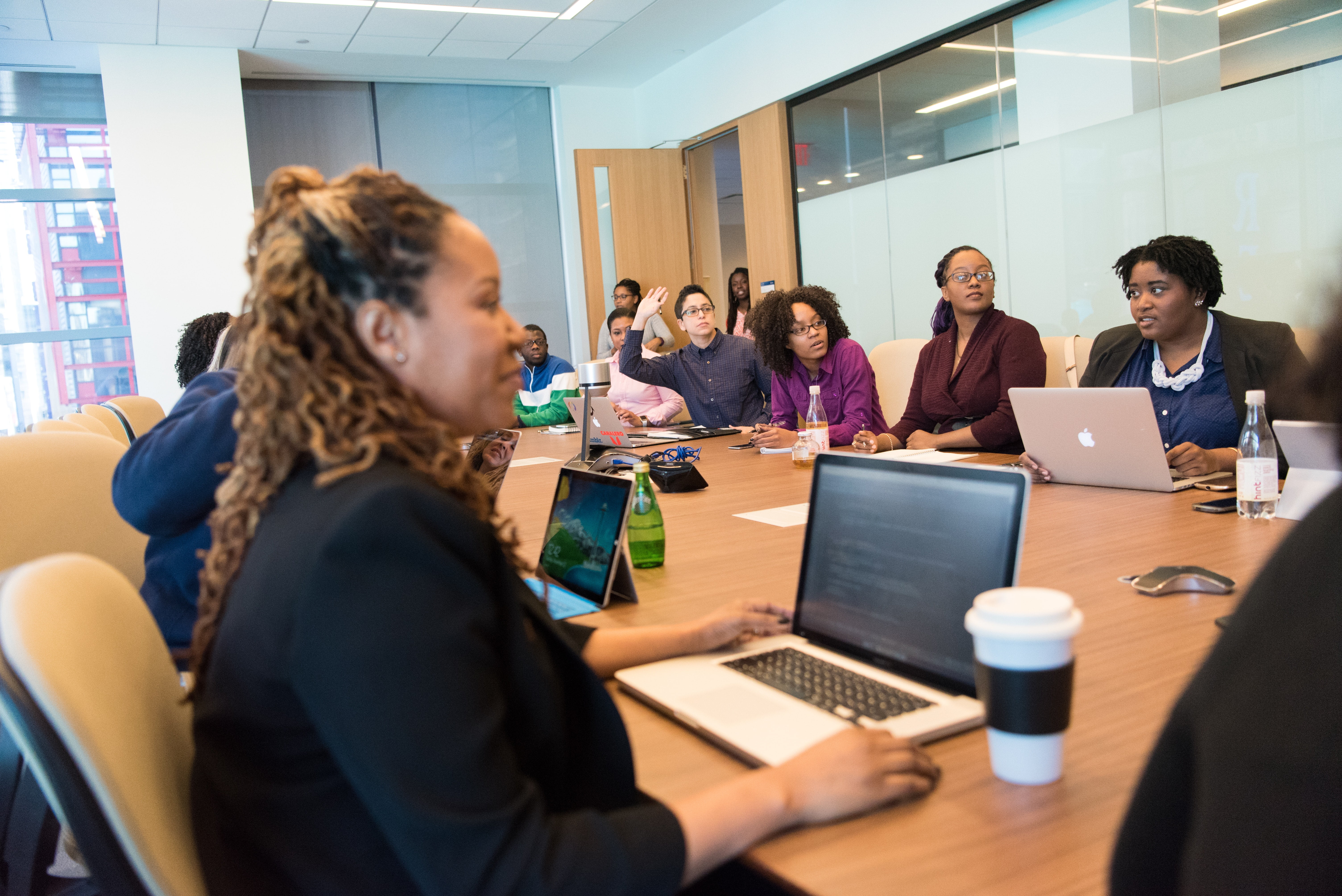 A room of adult employees work on laptops during a meeting in a boardroom.