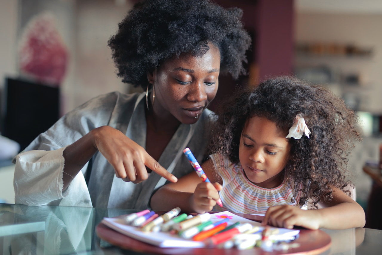 A teacher works on a coloring or art project with a young student in a classroom 