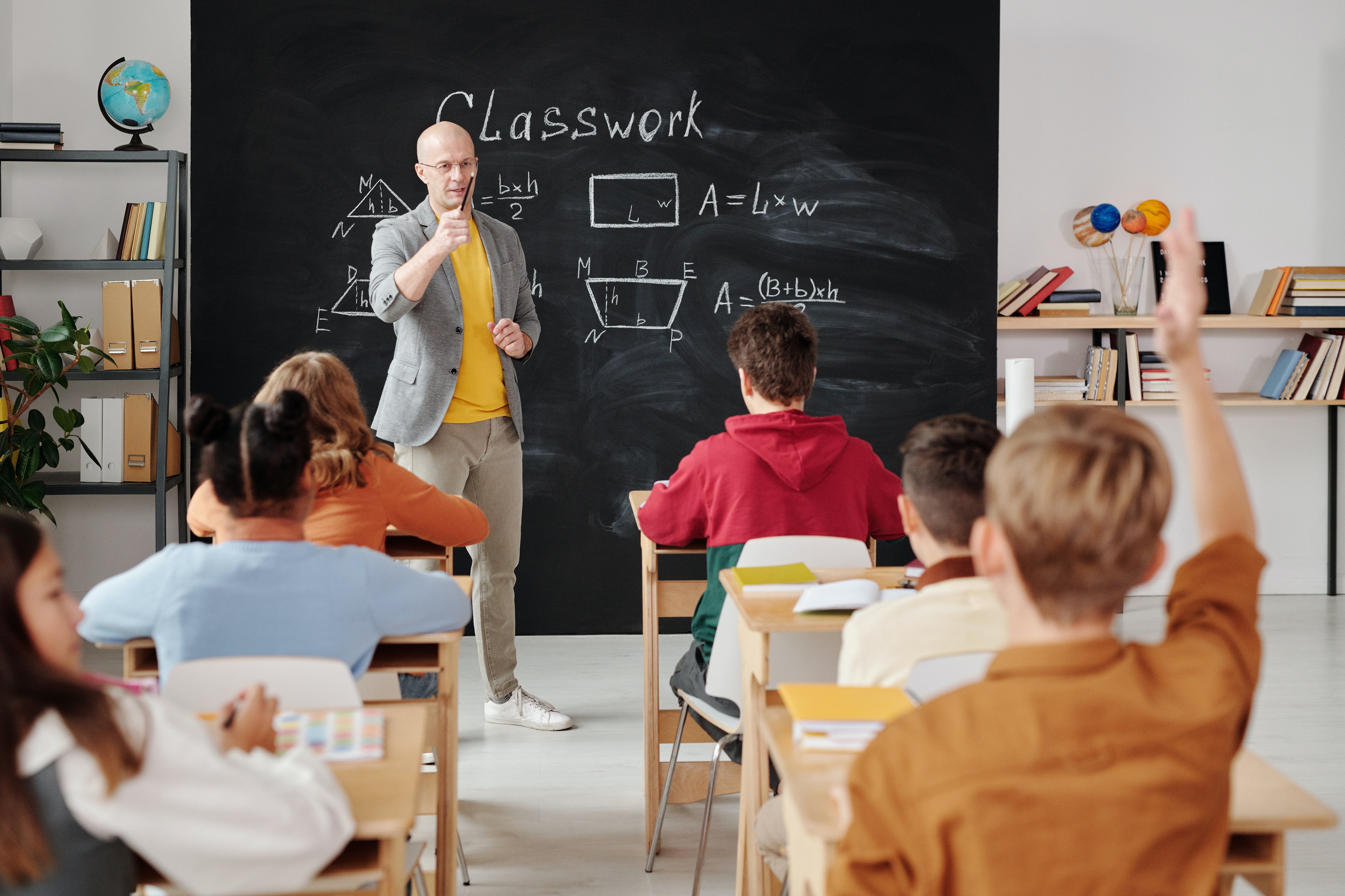 Teacher in a classroom with children with raised hands