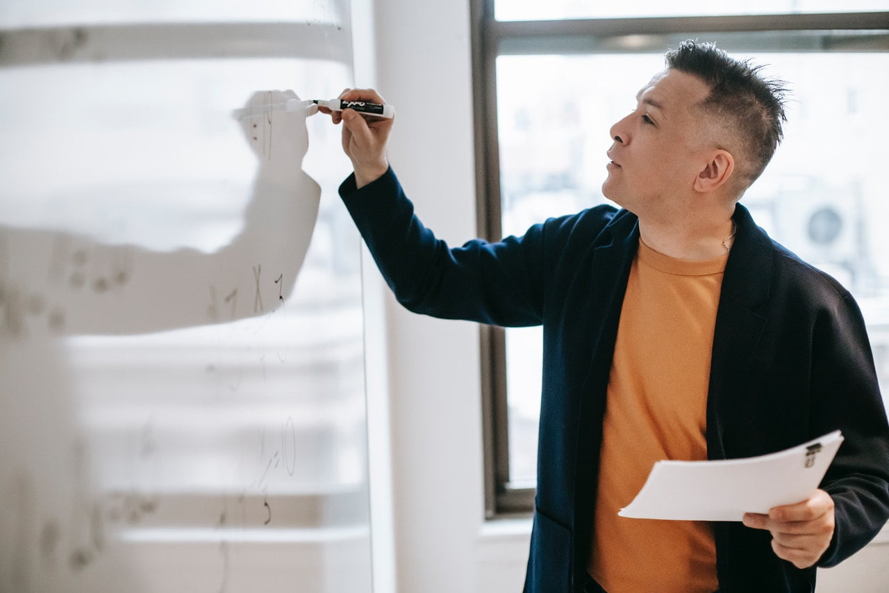 A teacher talks beside a whiteboard in a classroom