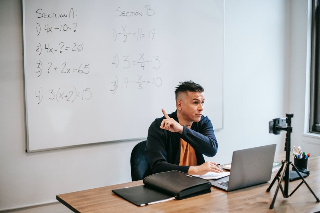 A teacher talks beside a whiteboard in a classroom