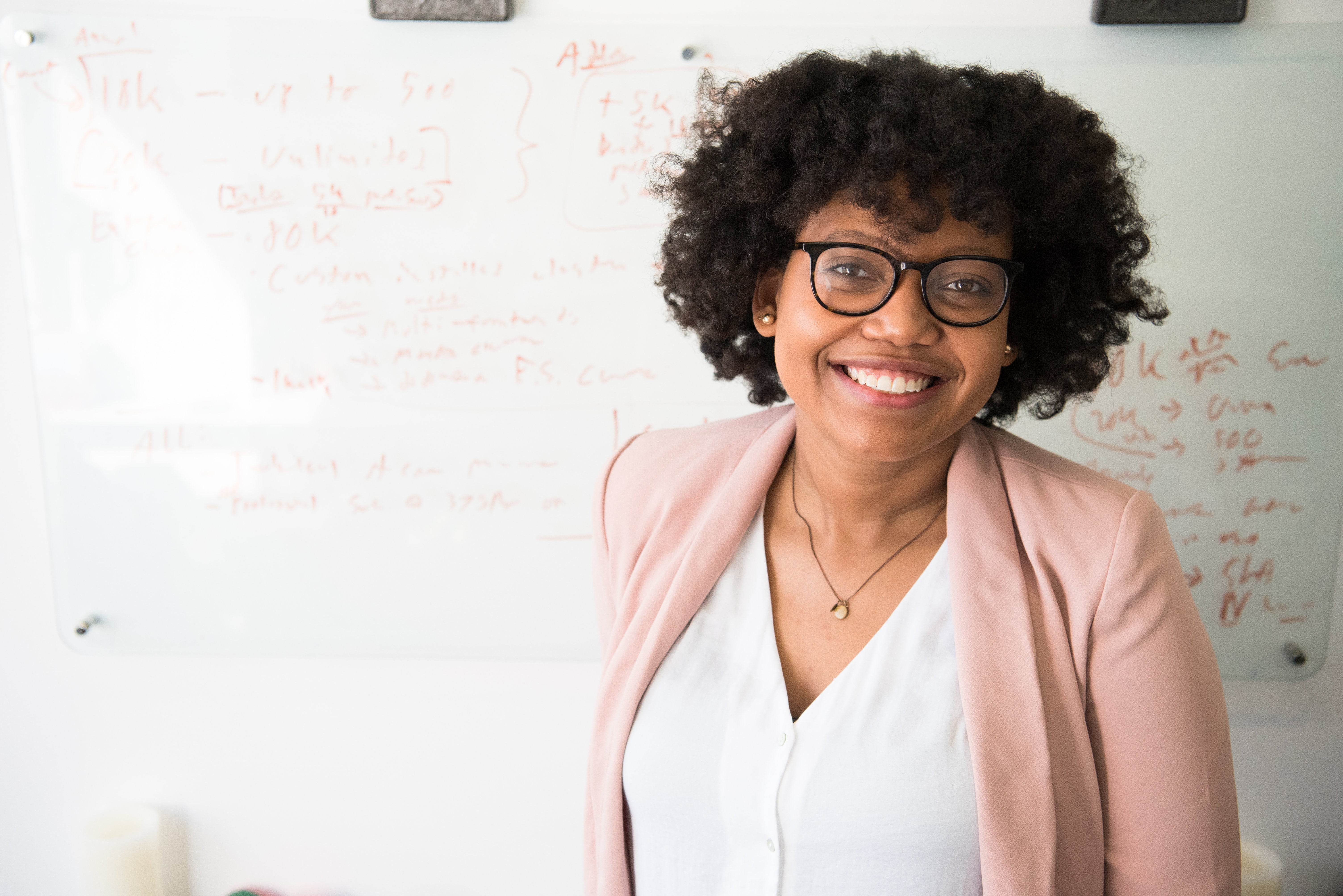 Teacher smiling for a photo while standing in front of a white board with classroom notes 