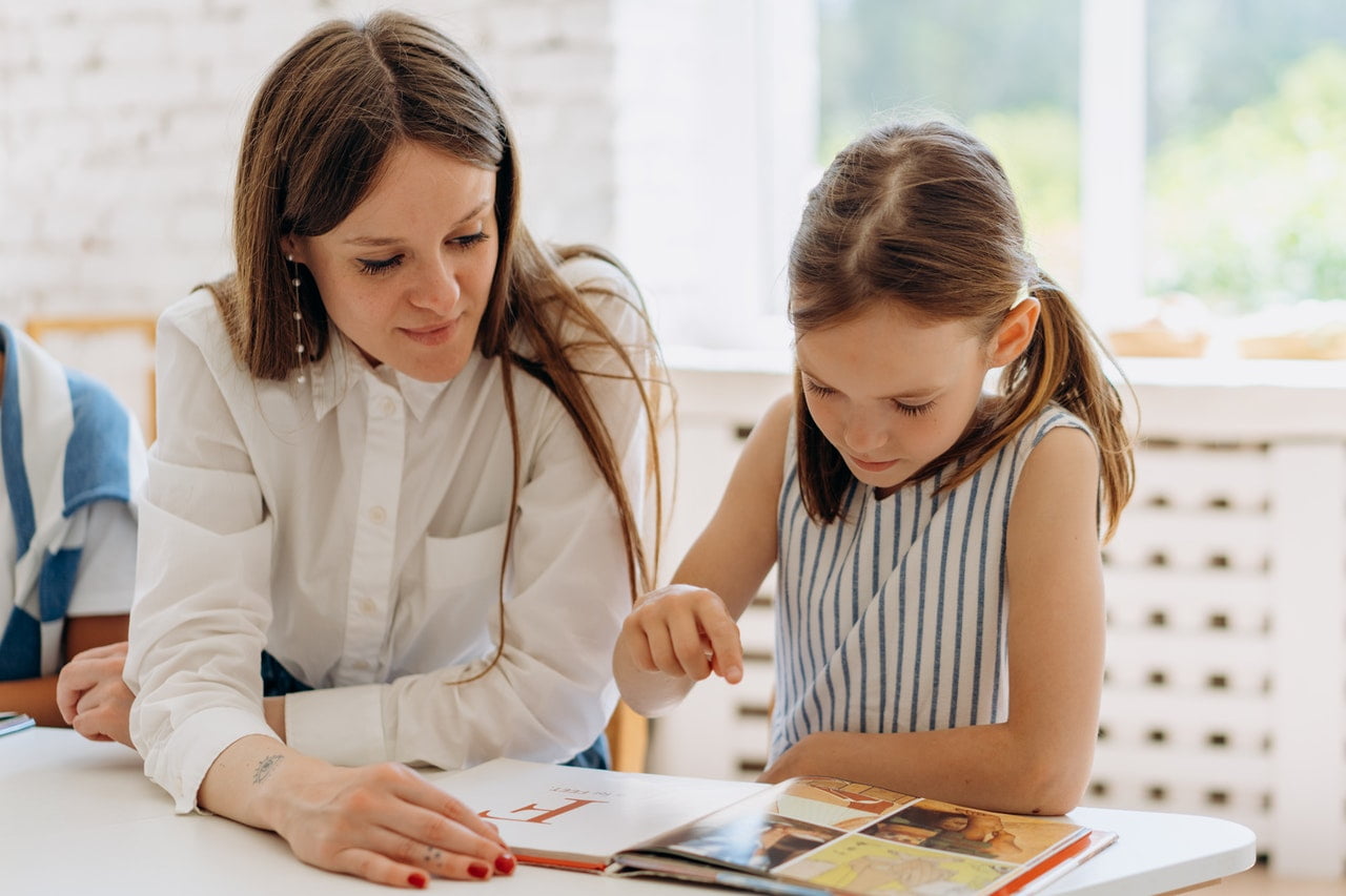 A teacher helps a young student read a book