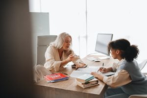 An educator sits at a desk with a student talking.