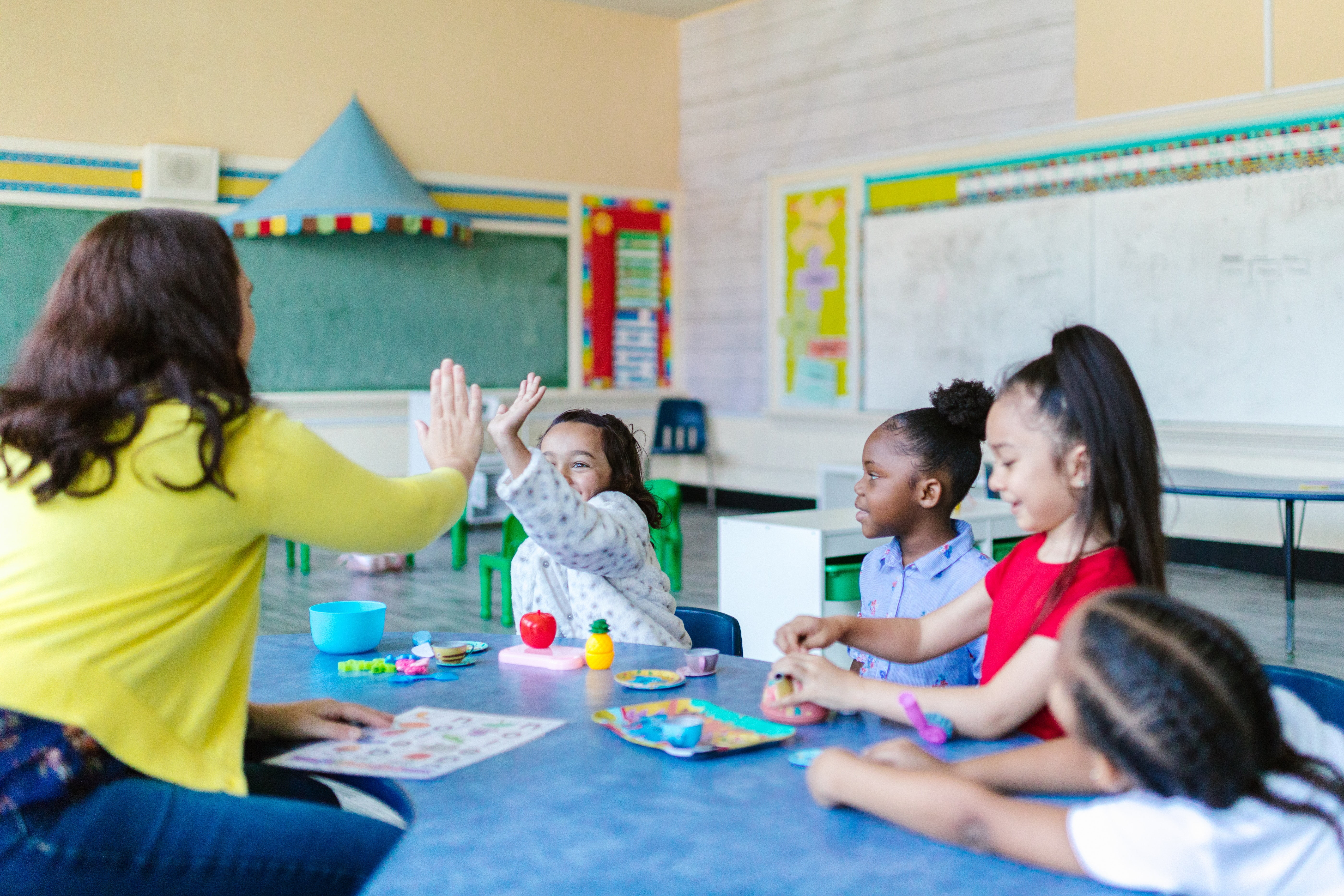 Teacher with students in a classroom. Teacher is giving one student a high five.