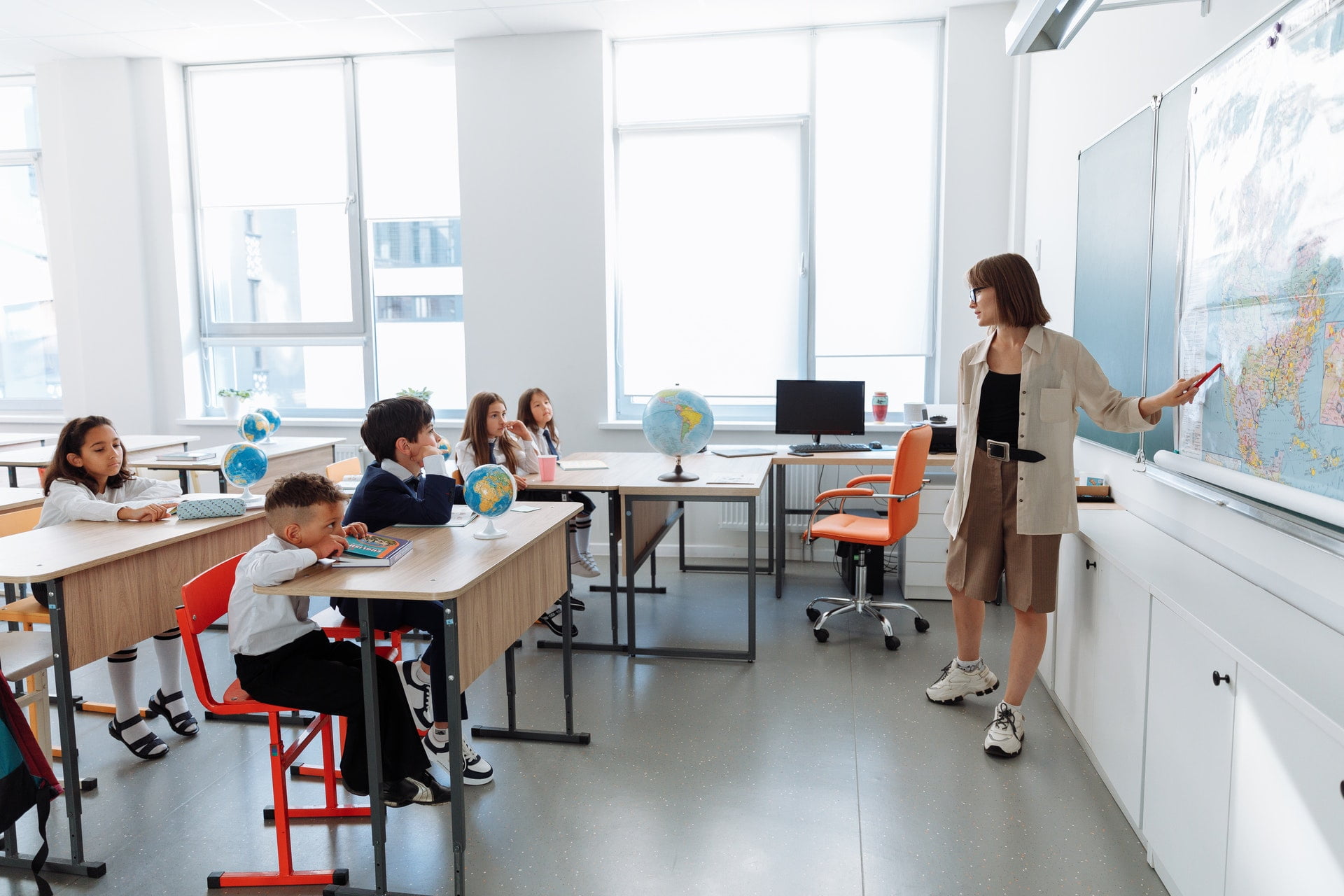 Teacher pointing at a world map with students in a classroom. 