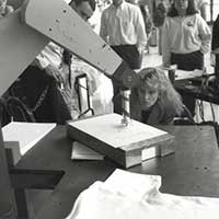 An engineering student watches as a robot arm draws on a page