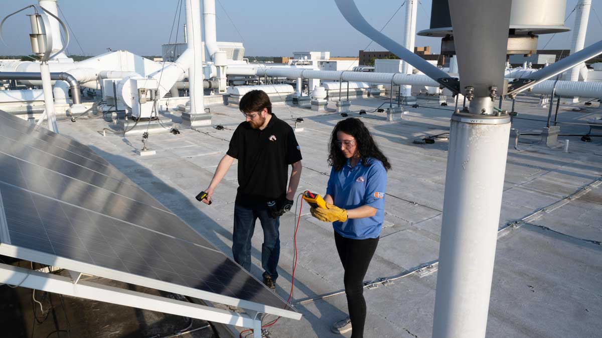 Researchers on a rooftop inspecting solar panels.
