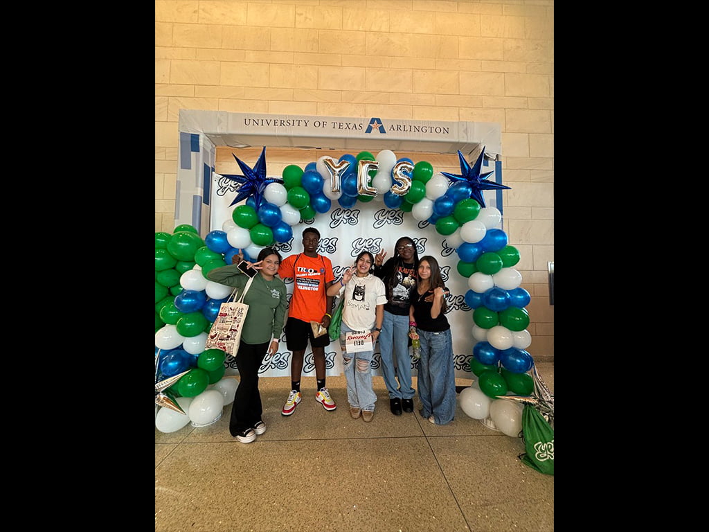a group of students under a shape of arch balloons