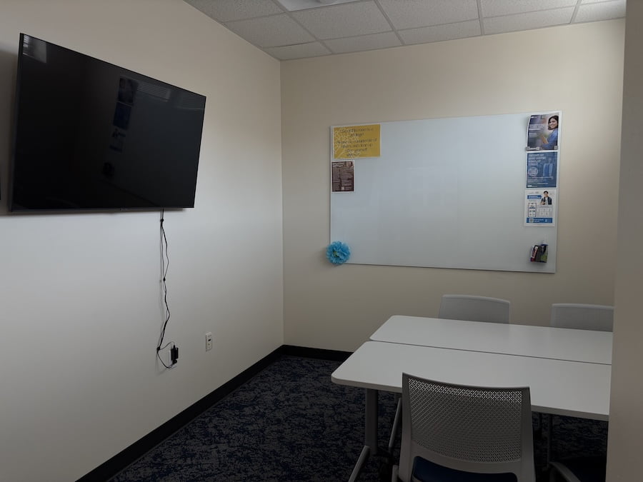room with a tv on the wall, a white board on the wall, and a table with chairs